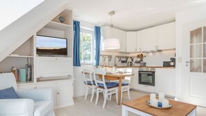 Eine moderne Küche mit weißen Schränken, einem Esstisch mit Stühlen und einem an der Wand befestigten Fernseher.