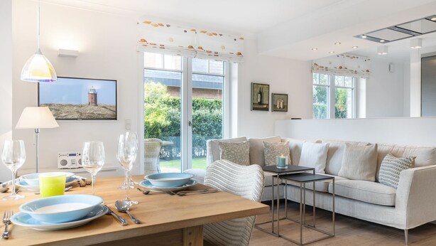 Un salon moderne avec une table à manger en bois, un canapé et un téléviseur. Il y a des fenêtres avec des rideaux, une lampe et un tableau au mur.