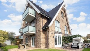 Une maison à deux étages, avec une façade en briques, de grandes fenêtres et un balcon.