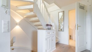 Eine Treppe mit weißer Geländer, ein weißer Konsolentisch mit Schubladen, ein Spiegel und eine Tür mit goldener Griff.