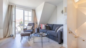 Ein modernes Wohnzimmer mit grauem Sofa, Sesseln und Couchtisch. Ein großes Schiebeglastür führt in einen Außenbereich.