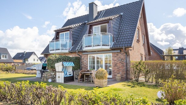 Ein zweistöckiges Haus mit Balkon, Garten und einem Fahrrad.