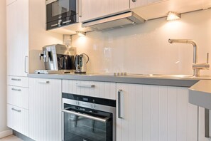 Ett modernt kök med vita skåp, en inbyggd ugn, en mikrovågsugn, en kaffebryggare och en diskho med en modern blandare.