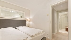 A hotel room with a bed, bedside lamp, and a mirror. There is a door leading to a bathroom with a shower.