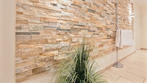 A bathroom with a stone wall, a floor lamp, and a potted plant.