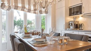 A modern kitchen with a wooden dining table set for a meal, a chandelier, and a view of the outdoors.