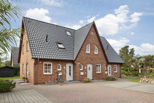 Een tweelaags bakstenen huis met een steil dak, een veranda en een fiets voor de deur.