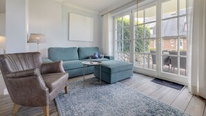 Ein geräumiges Zimmer mit großem Fenster, einer Couch, einem Sessel und einem kleinen Tisch.