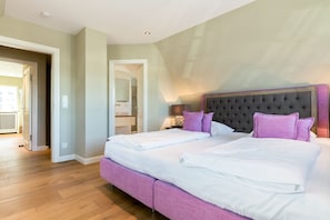 Un letto matrimoniale con testiera trapuntata, pavimento in legno e bagno visibile attraverso una porta aperta.
