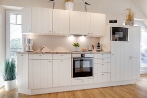 A modern kitchen with white cabinetry, a built-in oven, and a coffee maker. - Senskin - Das Appartement Senskin für 2 Personen in Ruhiger Lage in Westerland (Sylt)
