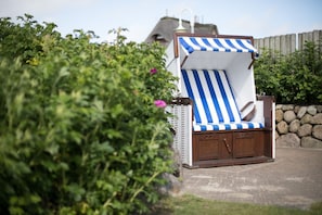 Une chaise de plage dotée d’un parasol à rayures bleues et blanches, placée à l’extérieur, avec un mur de pierres et de la verdure en arrière-plan.
