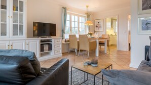 A modern living room with a TV, sofa, dining area, and kitchen. - Heide & Meer, App. 4 - Sylt. Heide. Und Meer (Wenningstedt-Braderup (Sylt))