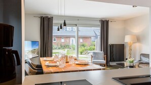 Ein modernes Hotelzimmer mit Essbereich, Fernseher und Blick auf einen Garten sowie ein Backsteinhaus.