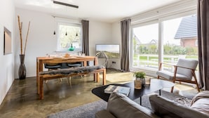 Ein geräumiges Wohnzimmer mit großem Fenster, einem Essbereich mit Holztisch und Stühlen, einer Couch und einem Couchtisch.