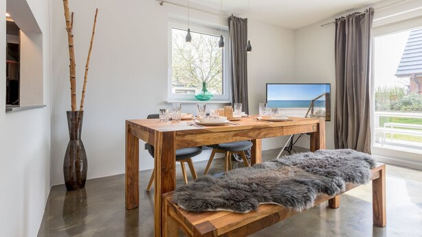 Ein moderner Essbereich mit Holztisch für vier Personen, einer Bank und einer Vase mit Zweigen.