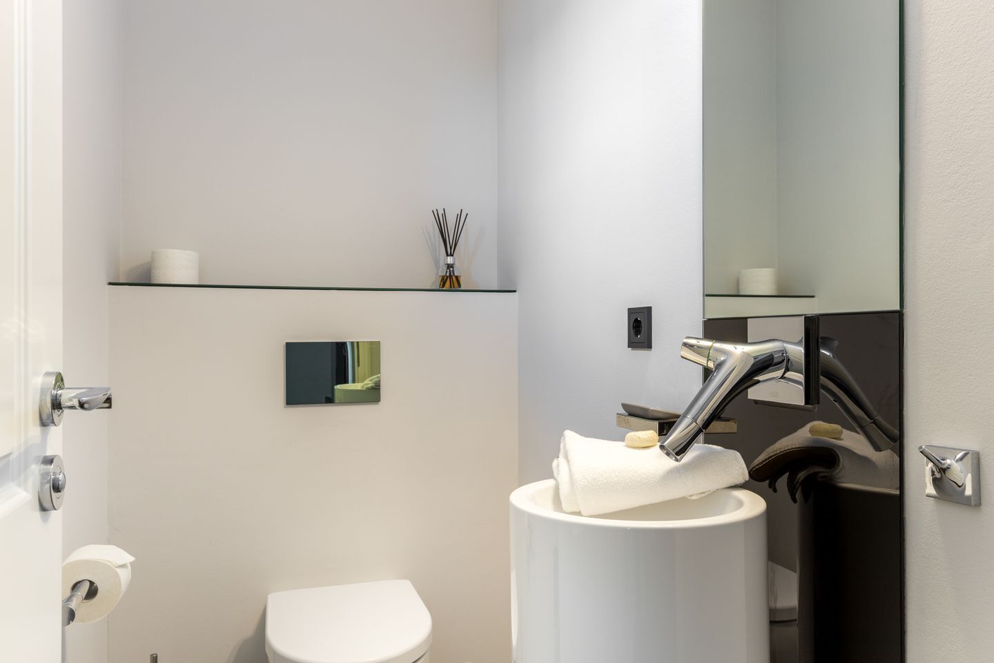 Un baño moderno con inodoro, lavamanos con toalla, espejo y repisas con artículos de aseo.
