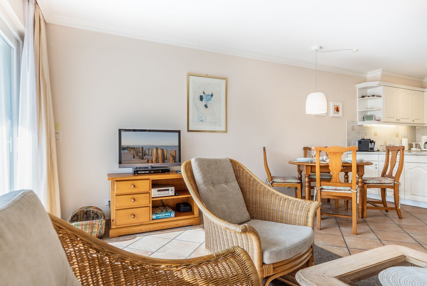 A living room with wicker furniture, a television, and a dining area with wooden chairs and a table.