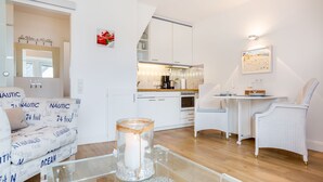 A modern kitchen with white cabinets, a dining area with a table and chairs, and a glass coffee table with a candle. - Syltblume, App. 11 - Viel Urlaub in Lauschiger Lage (Wenningstedt-Braderup (Sylt))