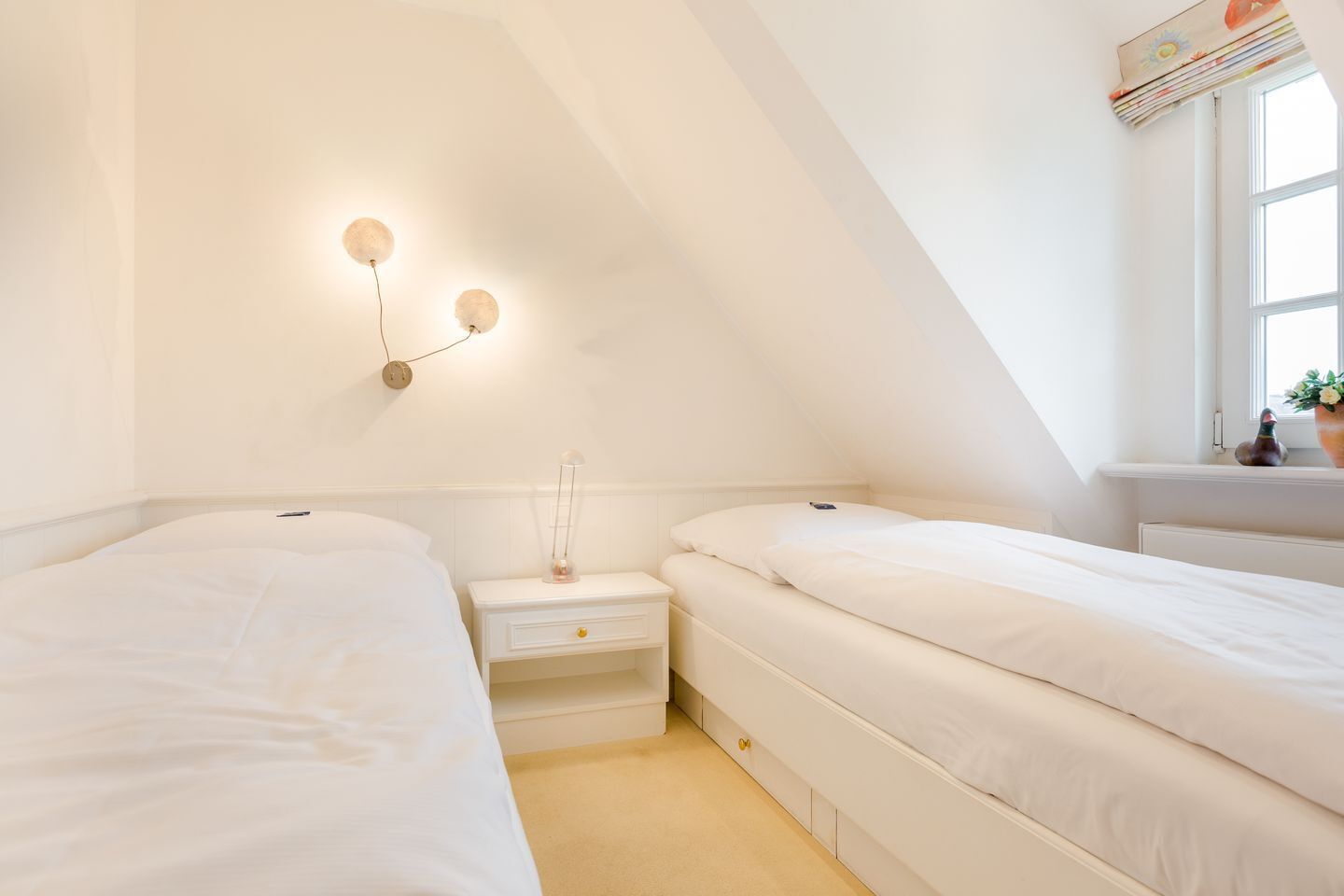 Ein Schlafzimmer mit zwei Einzelbetten, einem Nachttisch mit Lampe und einem Fenster mit Blick nach draußen.