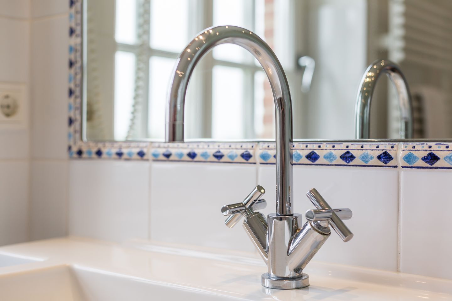 Een badkamer met een chromen kraan, een spiegel en blauwe tegels met een diamantpatroon.