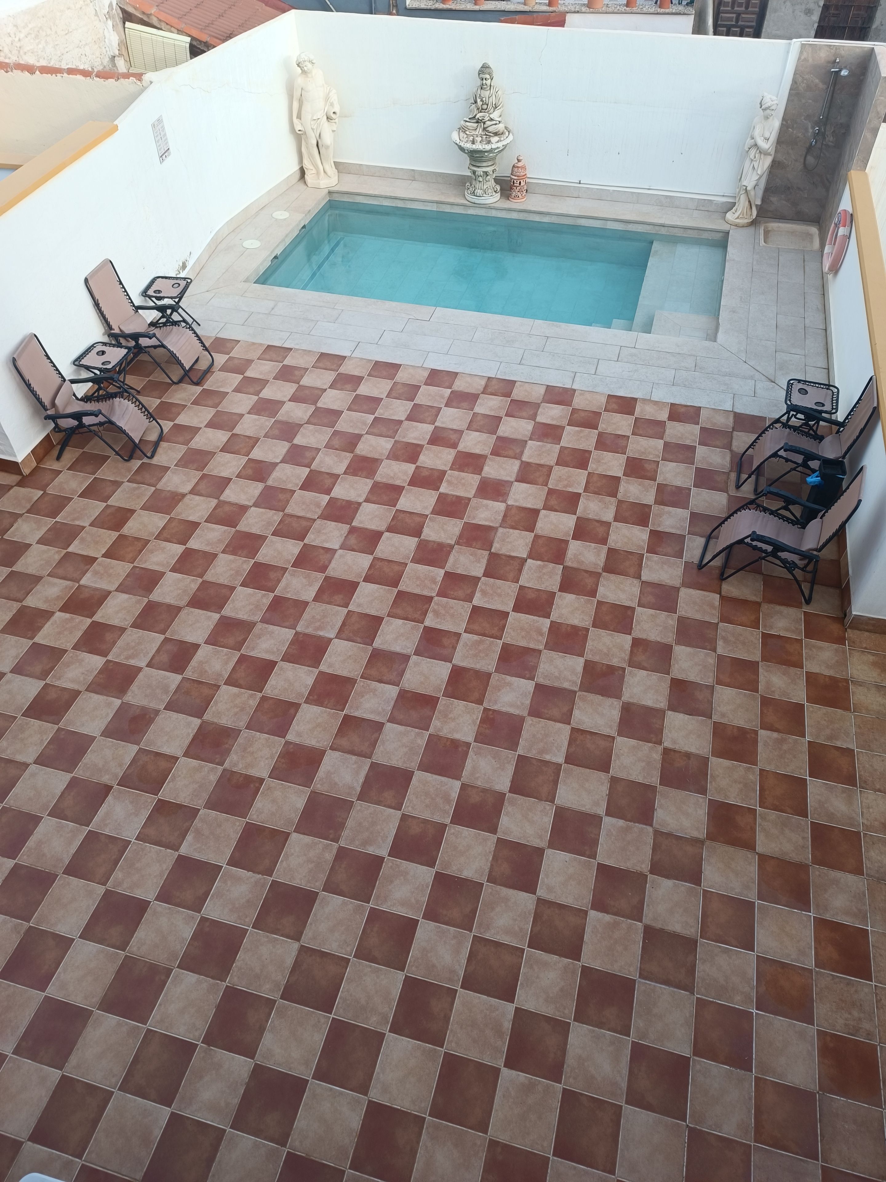 A rooftop pool area with checkered flooring, two lounge chairs, and a statue.