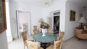 Un comedor con una mesa redonda rodeada de sillas ornamentadas, una araña y un jarrón con flores.