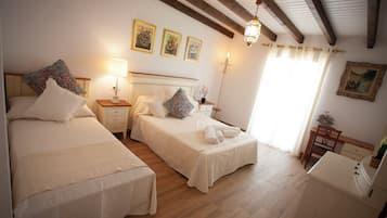 Een slaapkamer met twee bedden, een nachtkastje met een lamp, een bureau en een stoel. Er hangen drie ingelijste foto’s aan de muur en er is een kroonluchter.