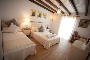 Un dormitorio con dos camas, una mesita de noche con lámpara, un escritorio y una silla. Hay tres cuadros enmarcados en la pared y un candelabro.