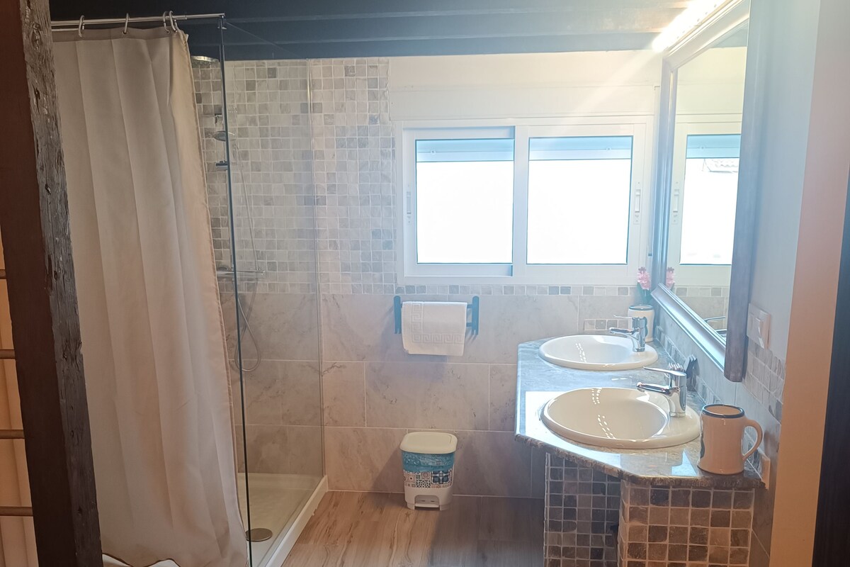 Uma casa de banho com chuveiro, duas pias, sanita e janela.