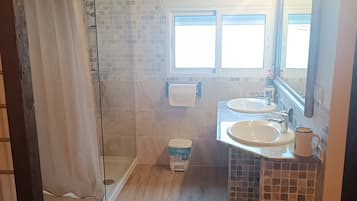 Un bagno con doccia, due lavandini, il water e una finestra.