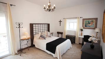 Una camera da letto con un letto, comodini, una scrivania, una sedia, una croce appesa al muro e un lampadario.