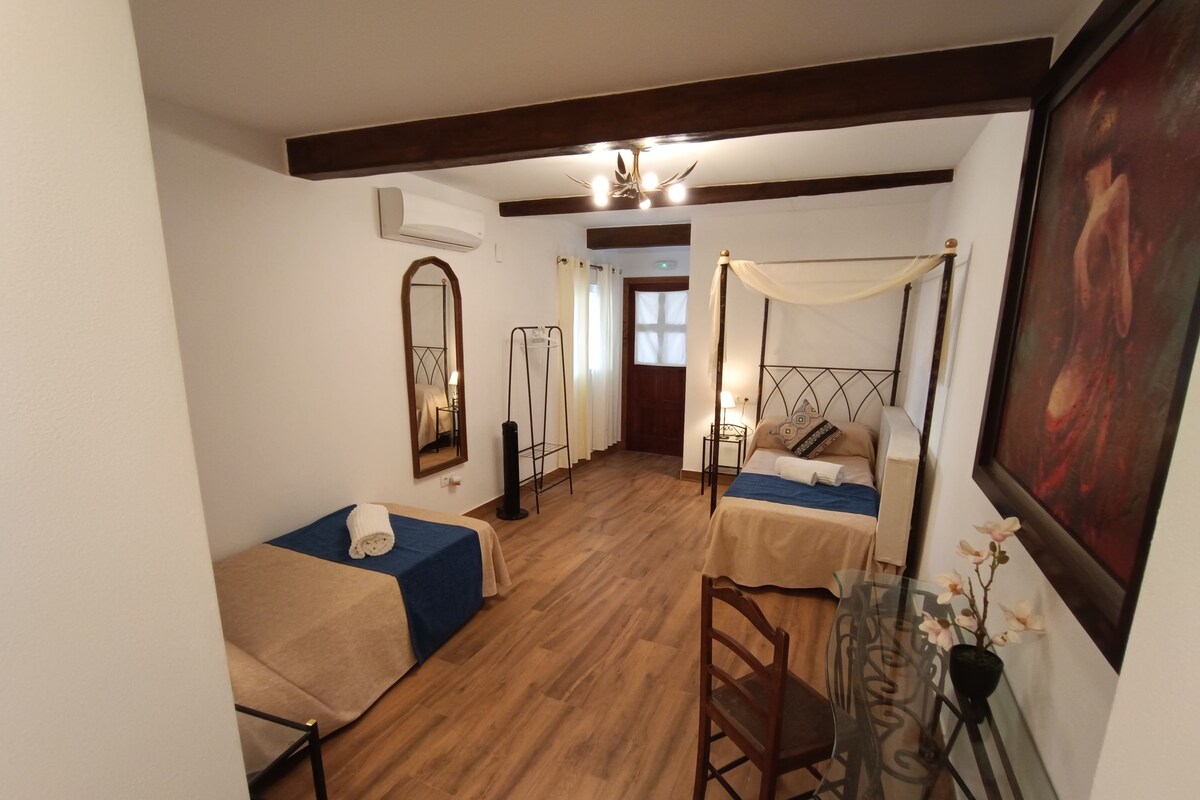 Quarto com duas camas, um espelho, uma mesinha com um vaso e uma janela com cortinas.