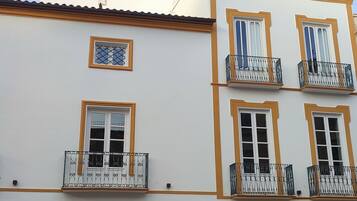 Un edificio con varios balcones, una entrada central y un patio con una piscina reflectante.
