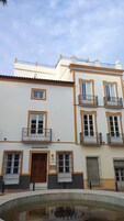 Un edificio con varios balcones, una entrada central y un patio con una piscina reflectante.