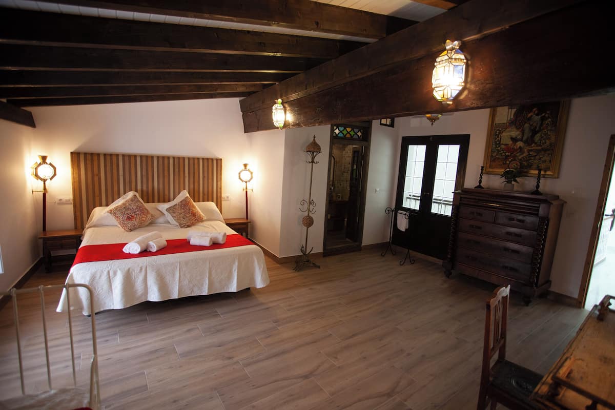 Ein Schlafzimmer mit einem großen Bett, Holzbalken, einem Schminktisch und zwei Wandleuchten.