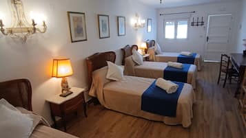 Camera d'albergo con tre letti, un lampadario e pavimento in legno.