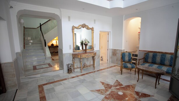 A spacious lobby with a marble floor, a grand staircase, a large mirror, and classic furniture.