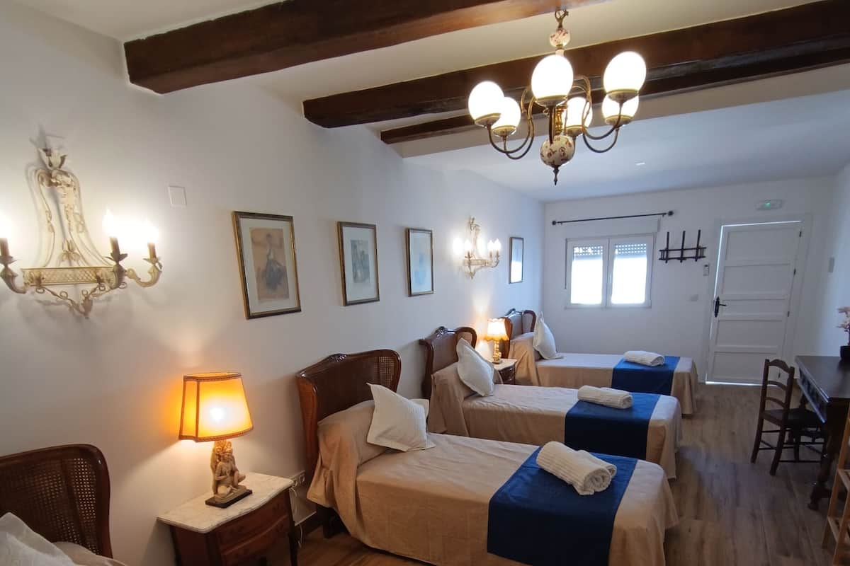 Ein Hotelzimmer mit drei Betten, einer Chandelüster und einem Holzboden.