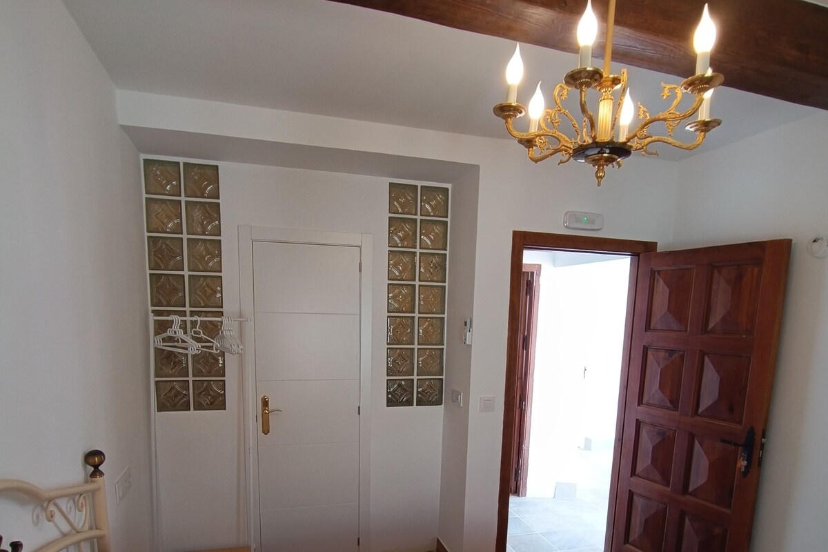 Quarto com cama, um candelabro, porta de madeira e janela com vista.