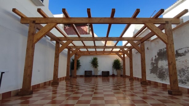 Un espace extérieur abrité, doté d’une pergola en bois, d’un sol carrelé et de plantes en pot.