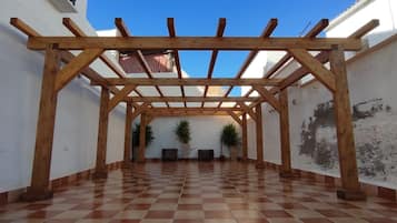 Zona exterior coberta amb una pèrgola de fusta, sòl de rajola i plantes en testos.