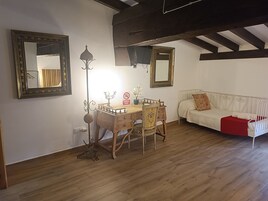 Una habitación con una mesa de comedor de madera, dos sillas, un sofá blanco y un espejo en la pared.