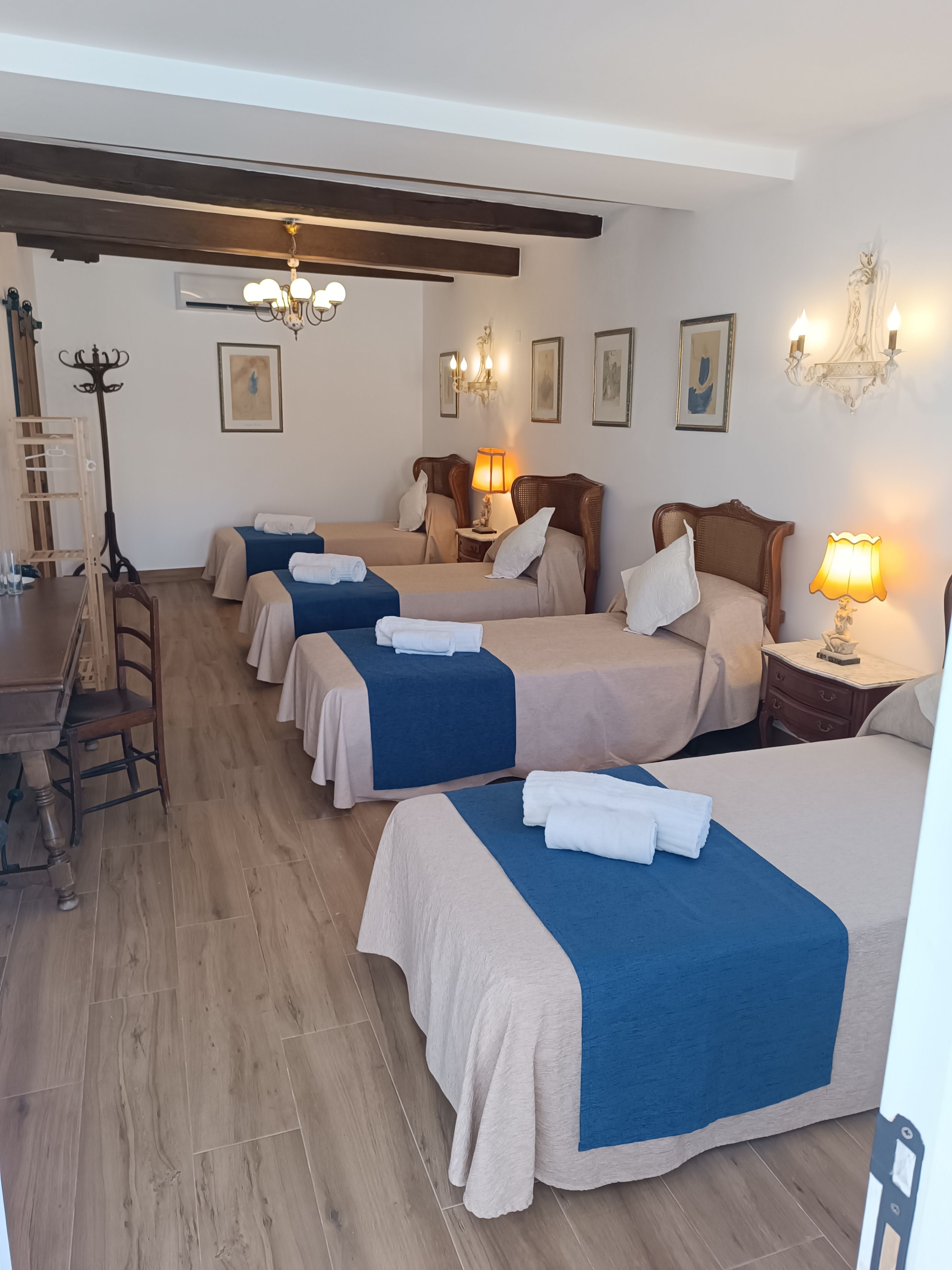 Una camera d'albergo con quattro letti, pavimento in legno, un tavolo da pranzo e lampade a parete.