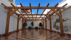 A covered outdoor area with a wooden pergola, tiled floor, and potted plants.