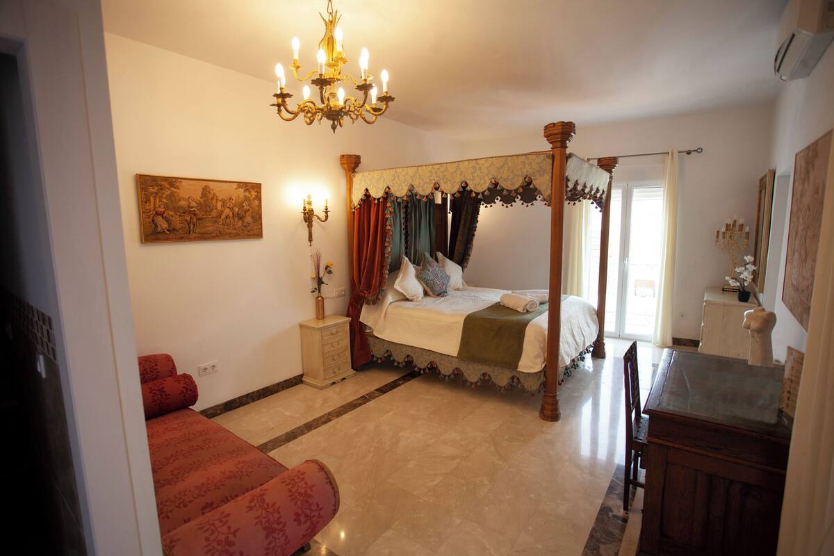 Ein Schlafzimmer mit einem Himmelbett, einer Kristallleuchter, einem Schminktisch und einem Schreibtisch.