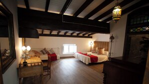 Une pièce avec un plancher en bois, un lit recouvert d’une couverture rouge, une table de chevet avec une lampe et une fenêtre laissant entrer la lumière du jour.