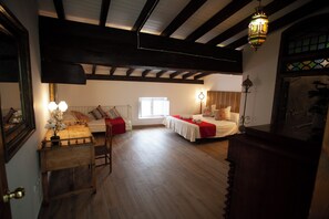 A room with a wooden floor, a bed with a red bedspread, a bedside table with a lamp, and a window with daylight. - El Palacete (Cuevas Del Almanzora)