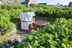 Ein Garten mit Korbmöbeln, einem Tisch und üppiger Bepflanzung, umgeben von einer Steinmauer.