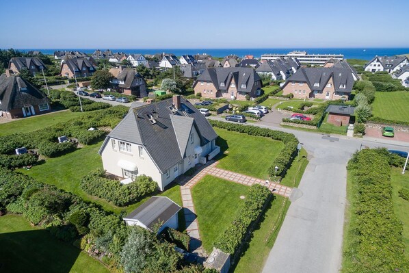 Luftaufnahme eines Wohngebiets mit Häusern, einem gepflegten Rasen und freiem Blick auf das Meer.