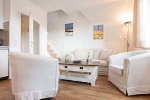 Ein modernes Wohnzimmer mit einem weißen Sofa, zwei Sesseln, einem Couchtisch und einem Gemälde von einem Leuchtturm.